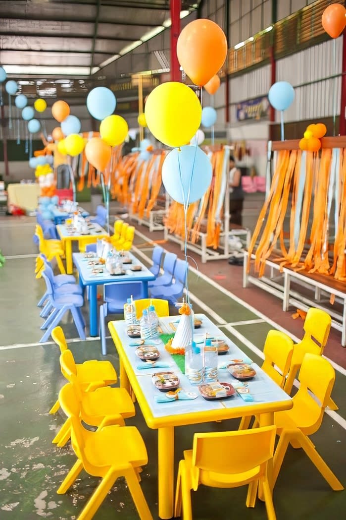 A colorful table set up in a warehouse adorned with vibrant balloons and whimsical tablecloths.