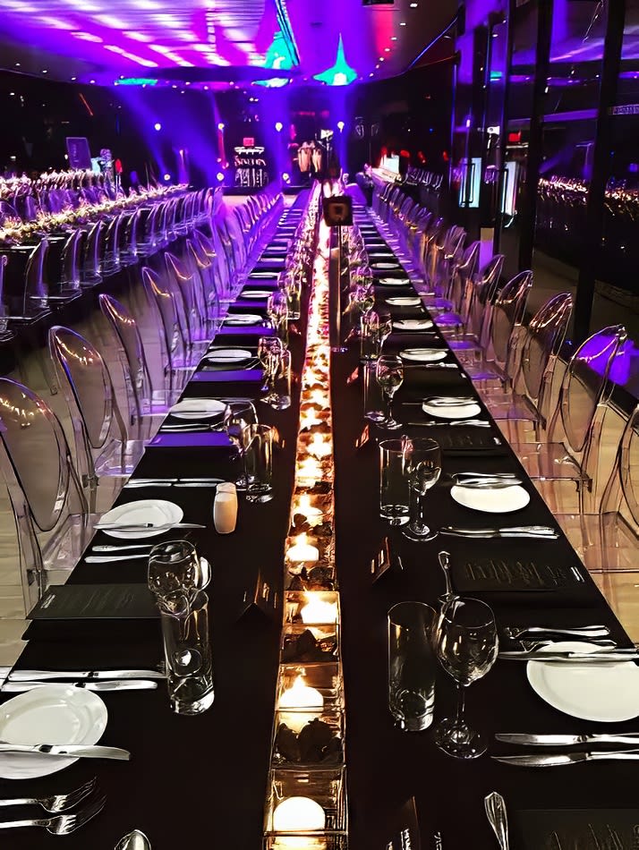 A large trestle table is set up in a dark room with candles, covered by a black tablecloth.