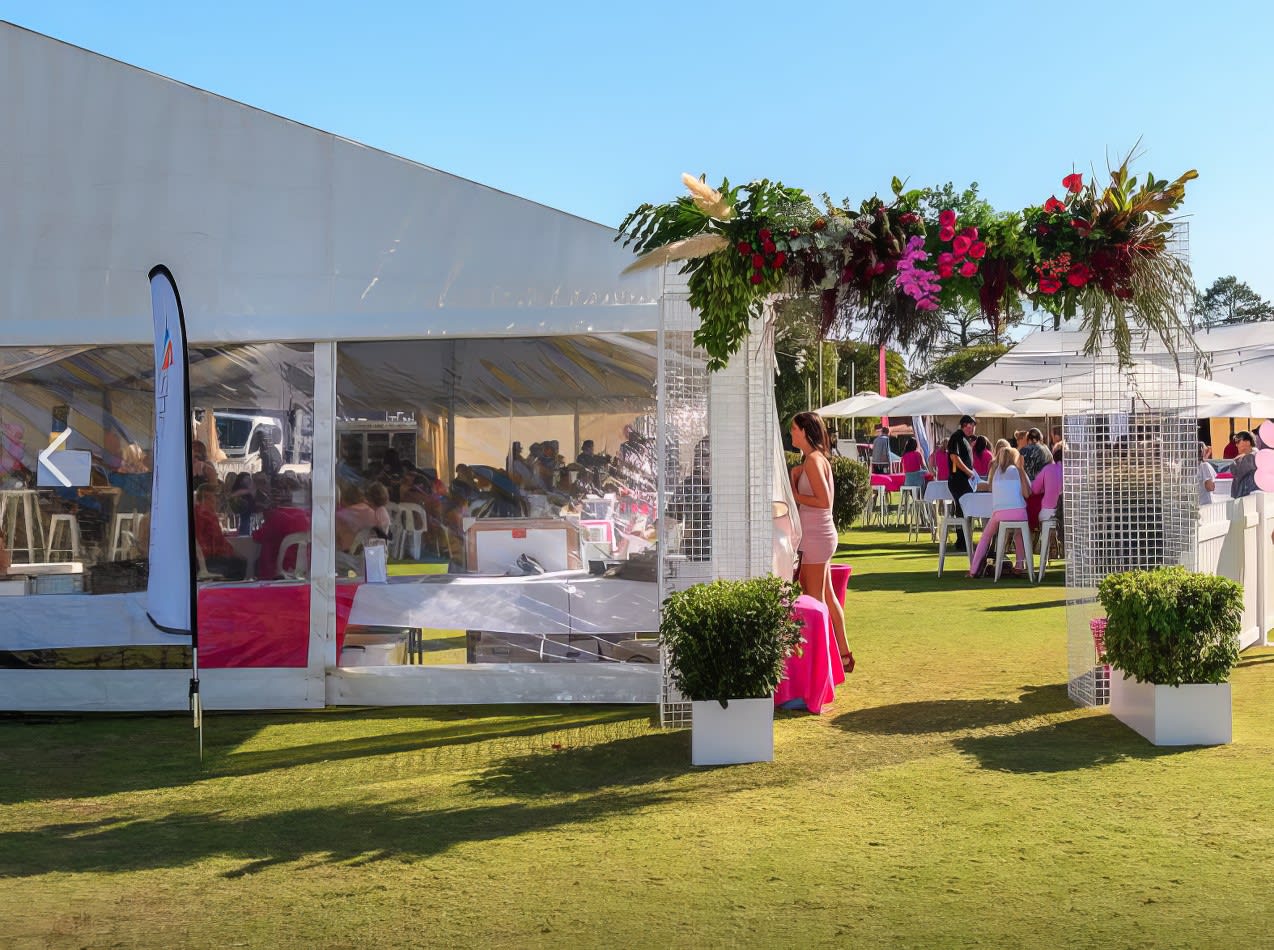 A white tent adorned with pink flowers in the middle of a grassy field, serving as an 8m x 24m - Framed Marquee.