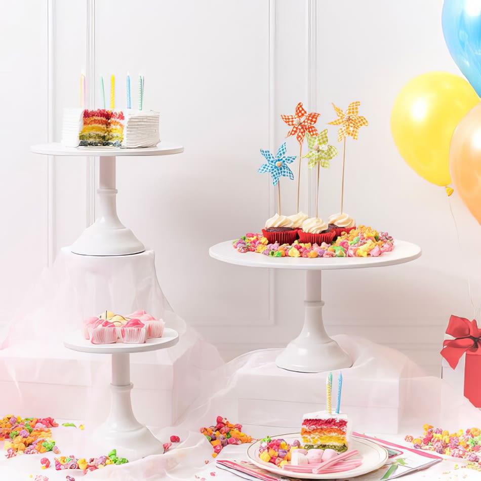 A birthday cake on a white metal cake stand with balloons and confetti.