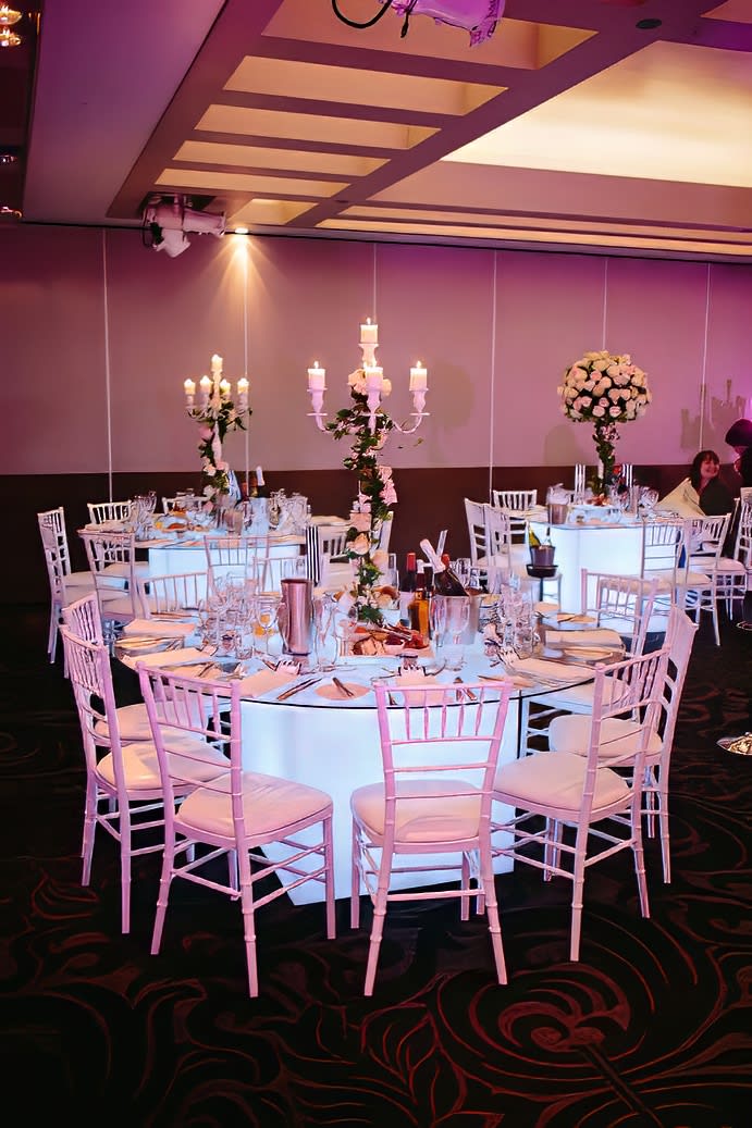 A square room with white tables and chairs hired for an exquisite banquet.