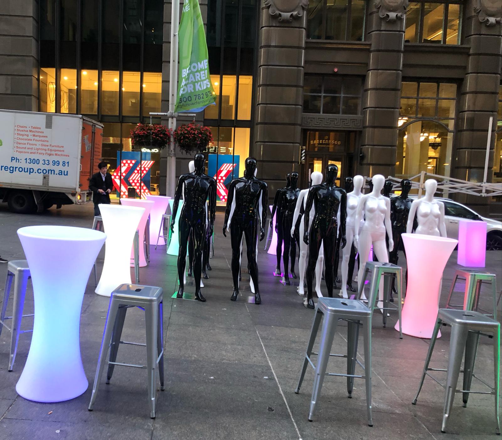 A group of mannequins in front of a Silver building.