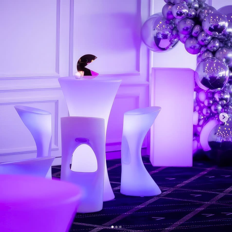 A purple LED cocktail bar table and chairs in a glowing room.