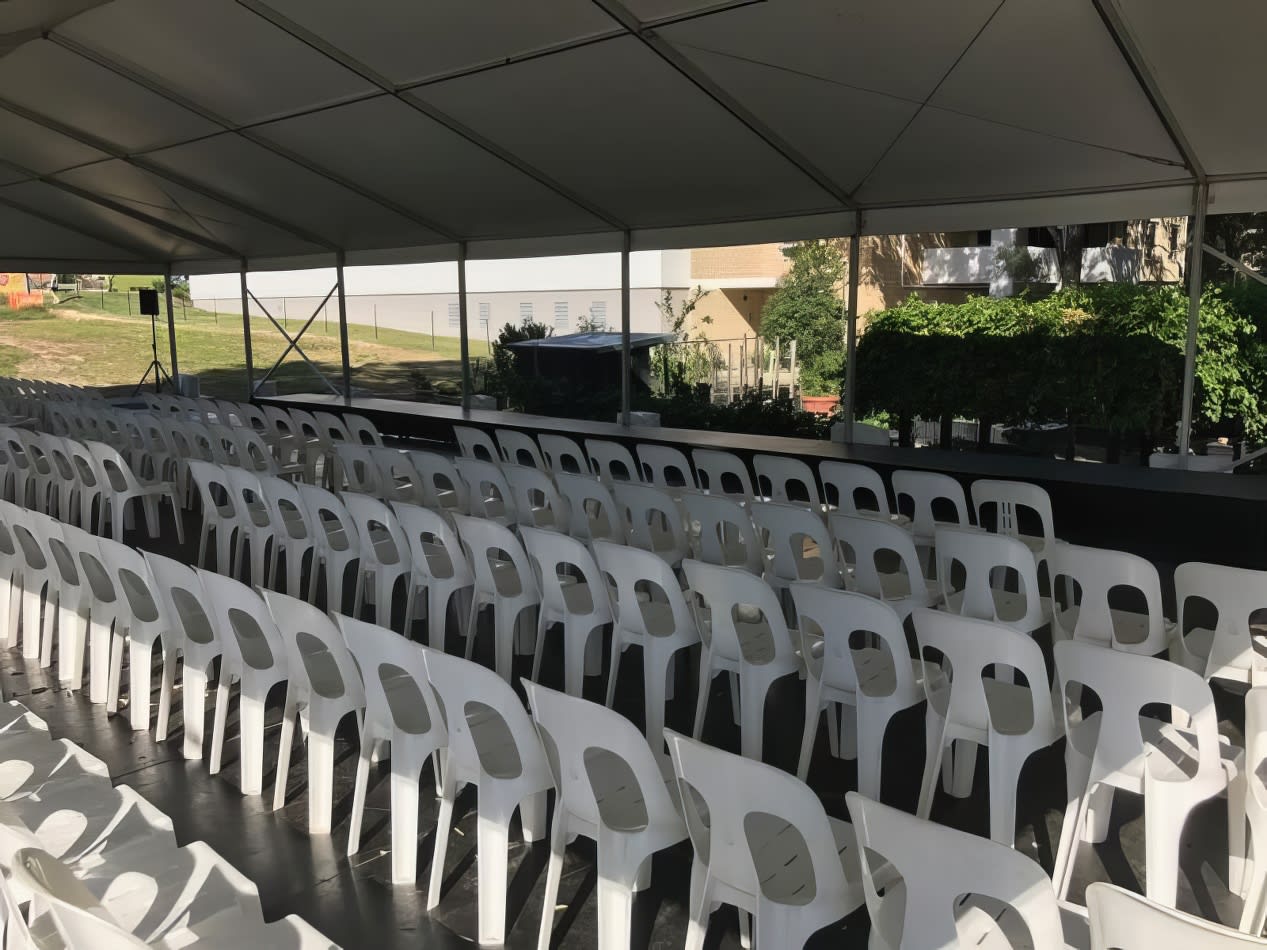 A large tent with rows of white plastic stackable chairs.