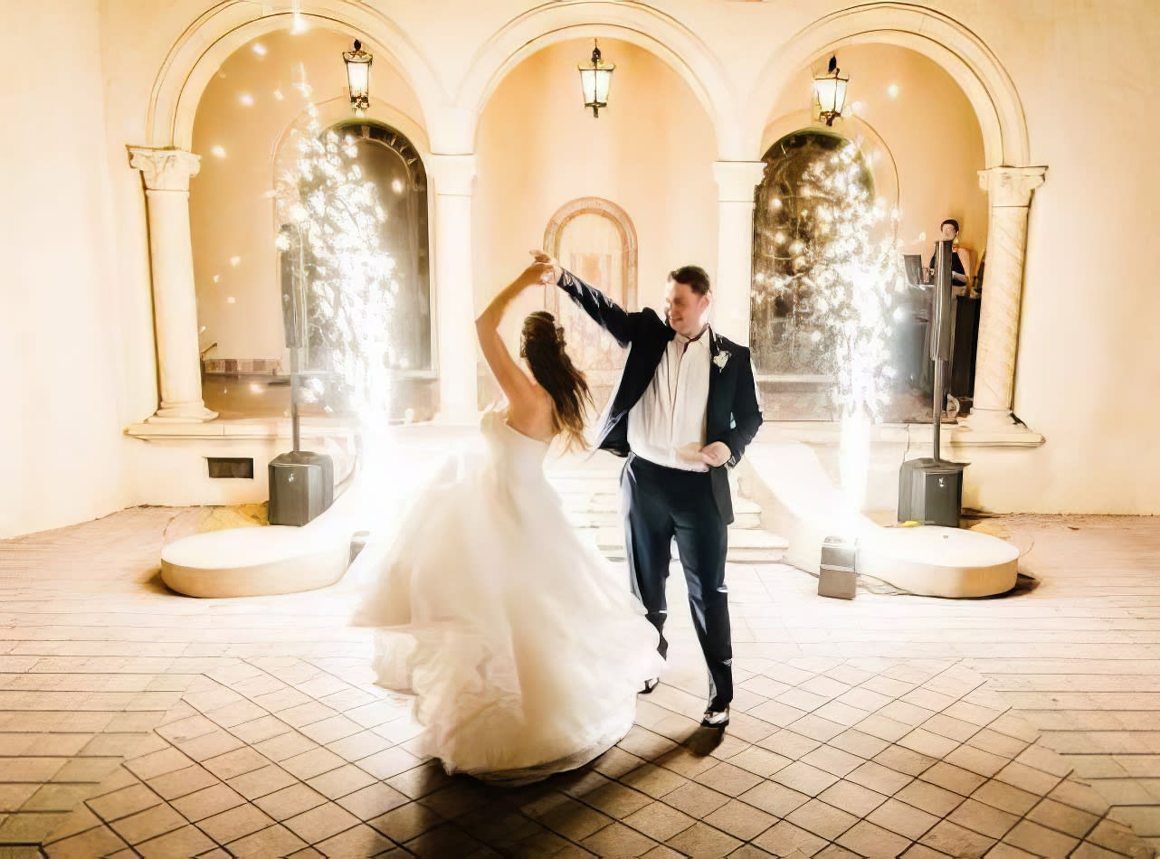 A bride and groom dancing with dry sparklers in front of an archway.