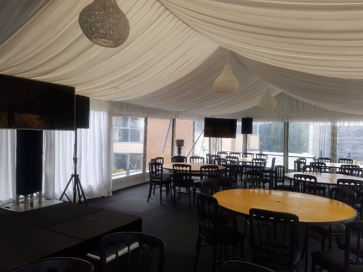 A white tent with tables and chairs in it illuminated by white pendant rope lights.