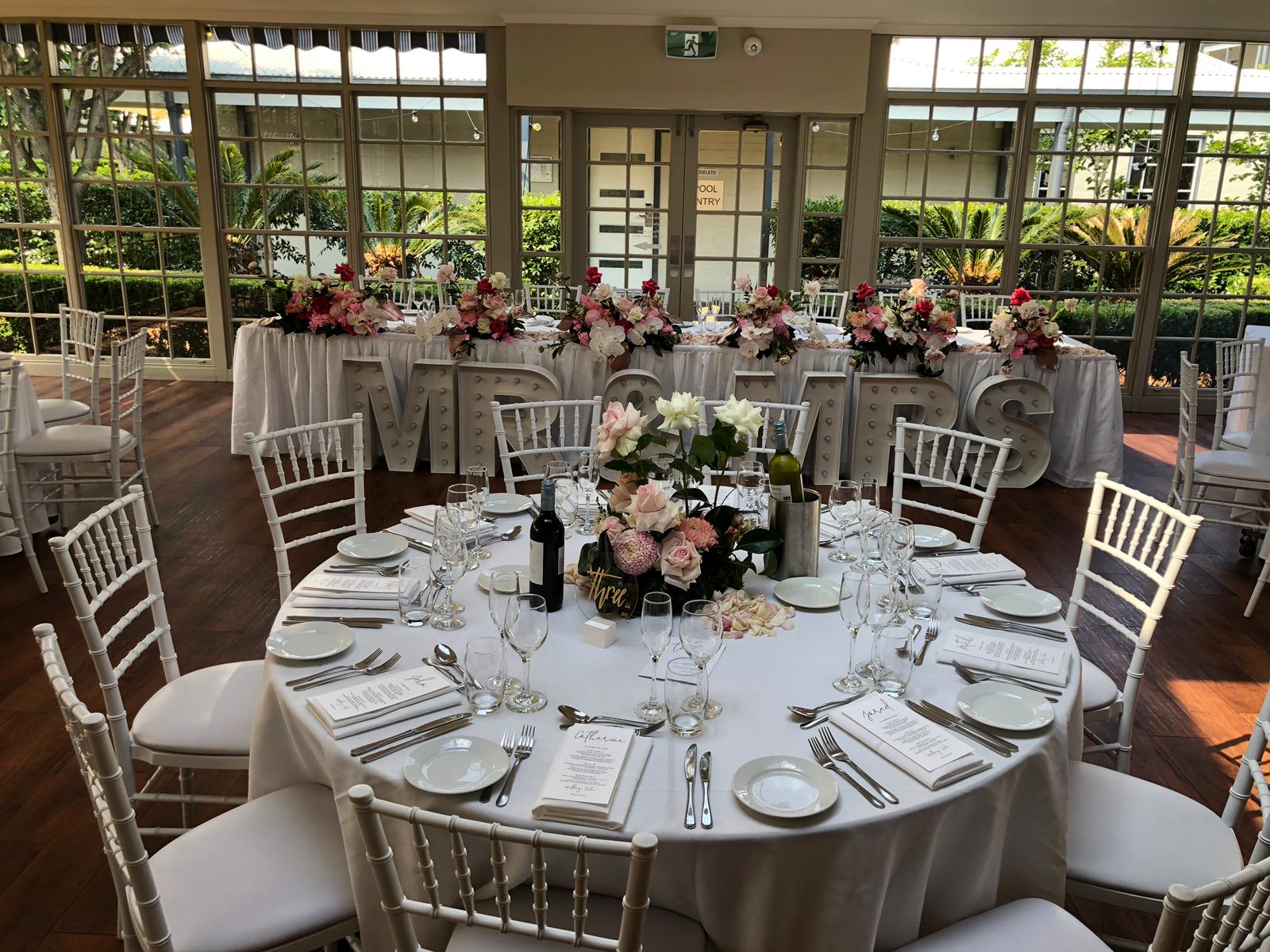 A table set up with white Tiffany chairs and flowers.