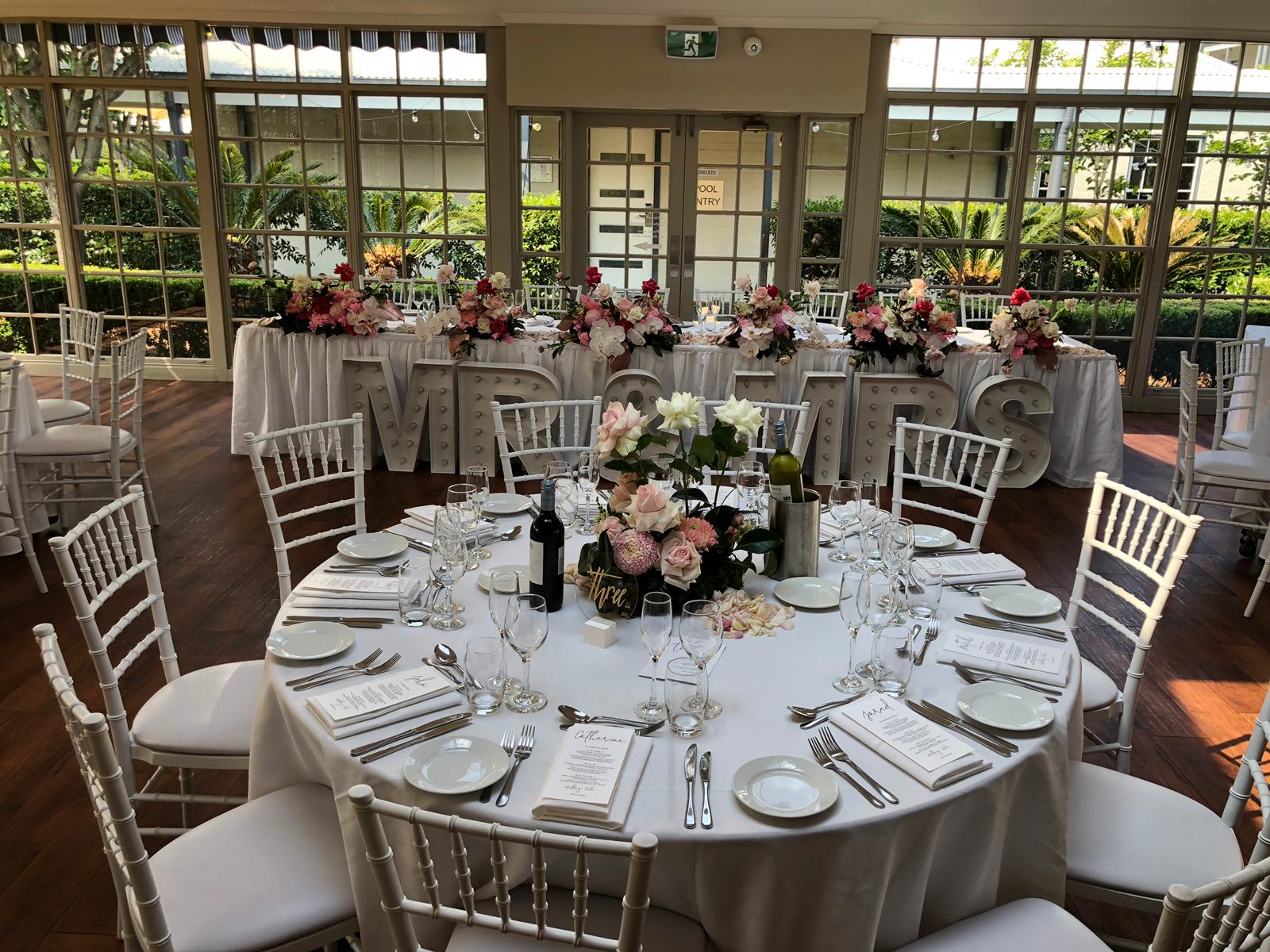 A table set up with white Tiffany chairs and flowers.