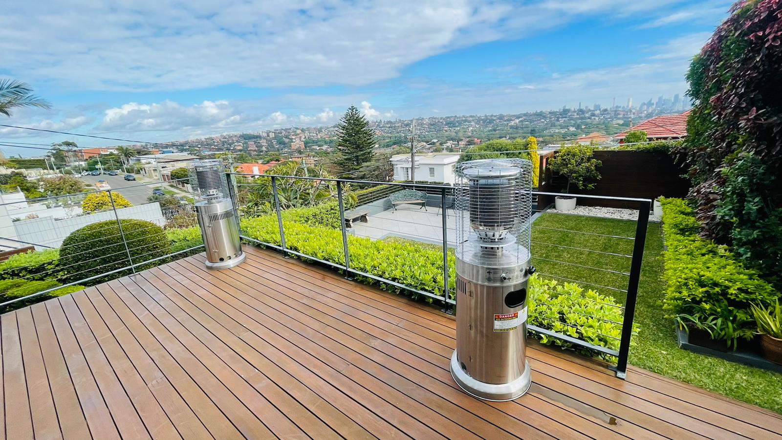 A wooden deck with two outdoor heaters and a city view.