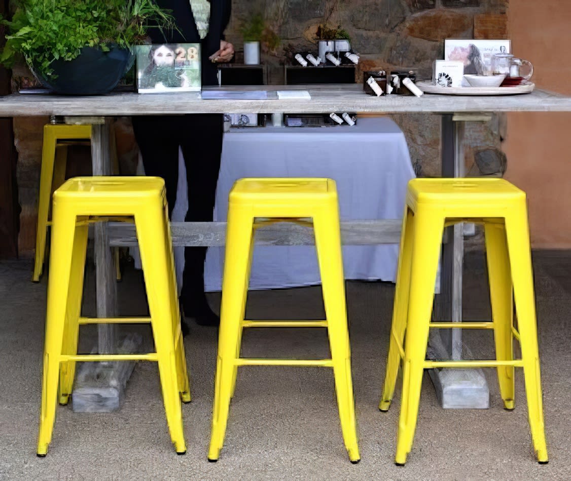 A group of yellow Tolix stools in front of a table.