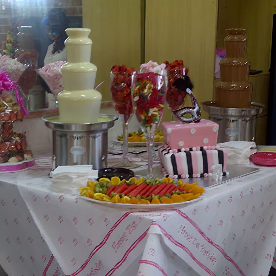 A table with a chocolate fountain and a large fruit platter featuring in-season fruit.