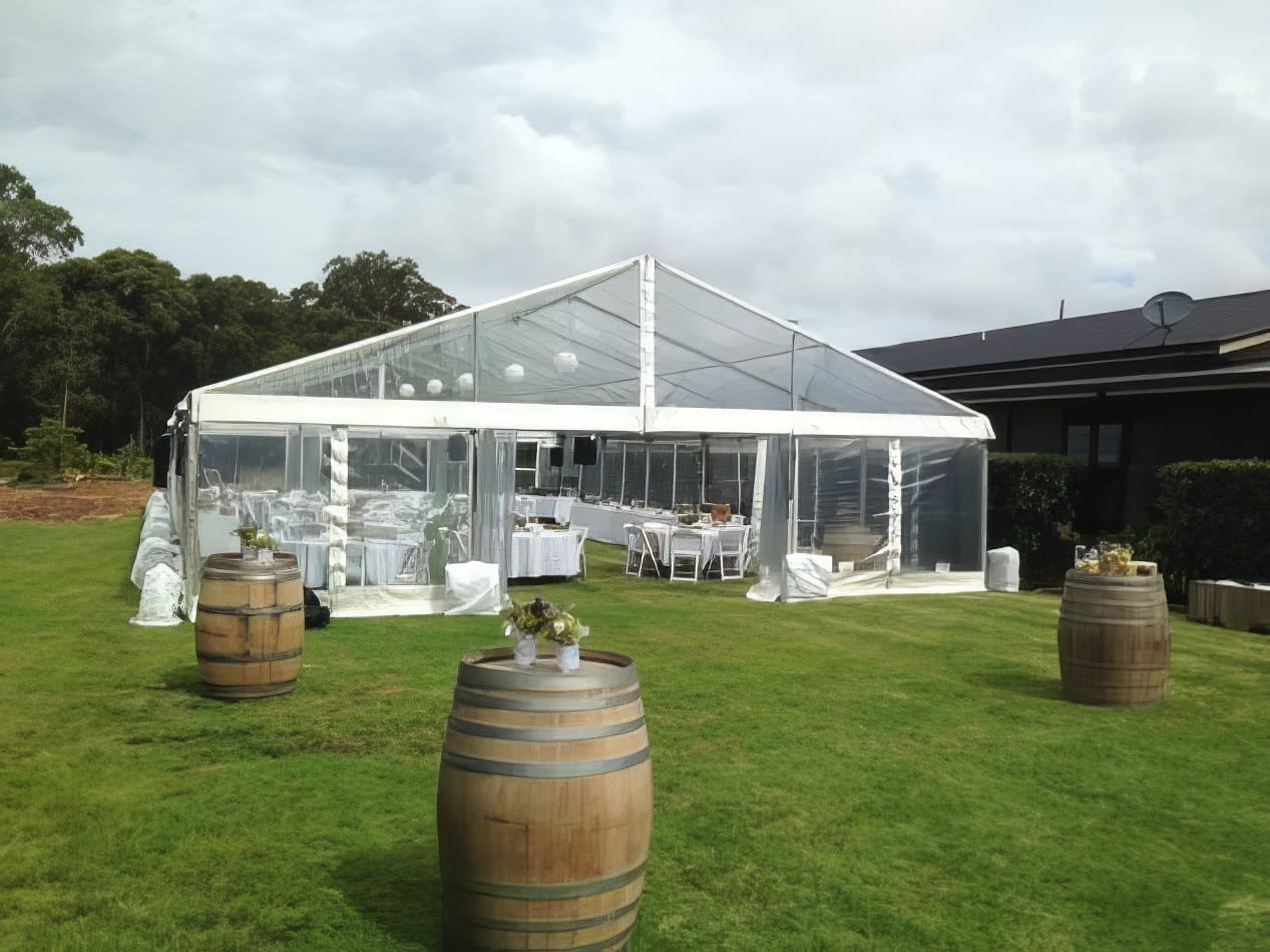 A white framed marquee tent set up in a grassy area with wine barrels.