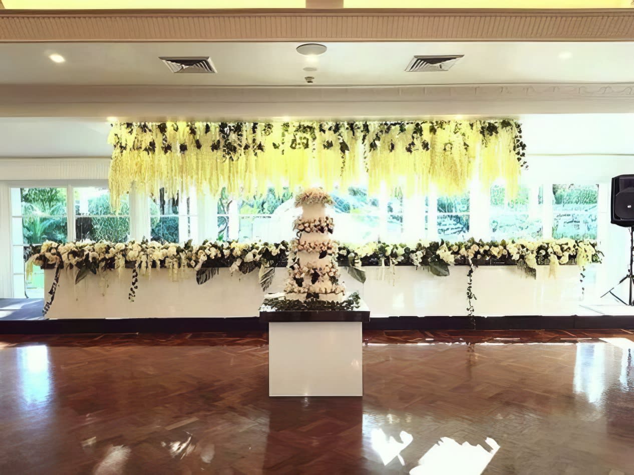 A glossy wedding cake adorns a beautifully decorated table in a spacious room.