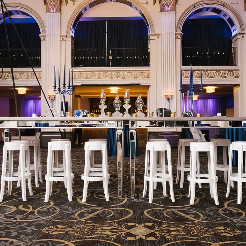 An ornate ballroom with ivory stools and a bar.