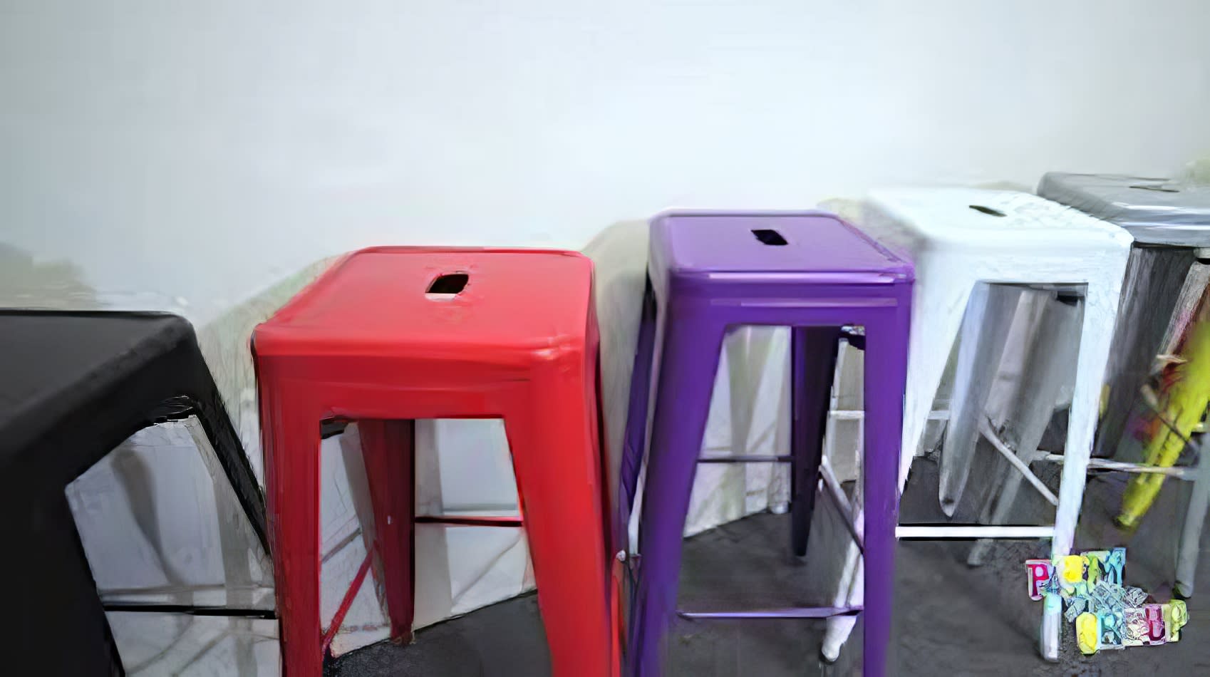 A row of colorful metal stools, including purple Tolix stools, in a room.