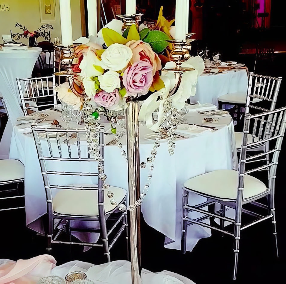 A table with silver Tiffany chairs and flowers on it.