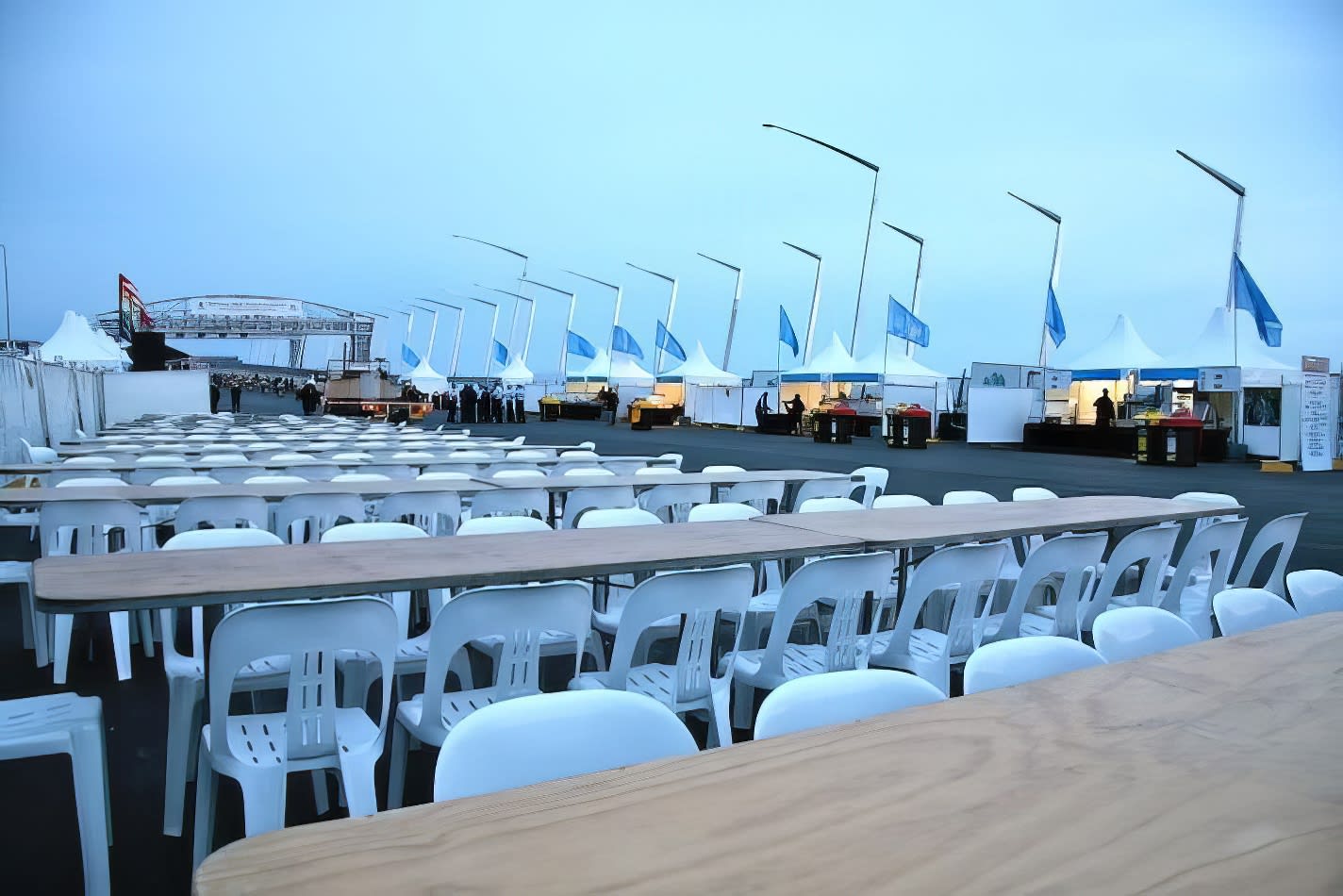 White tables and chairs, including Timber Trestle Table 2.4m Hire, are set up in front of a tent.