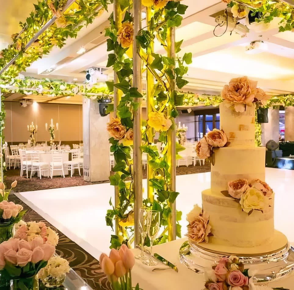 A large wedding cake is sitting on a table in a room filled with flowers.