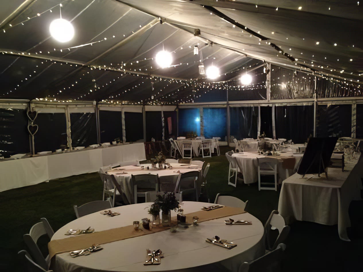 A tent with tables and chairs set up for a wedding reception, adorned with elegant white rice lanterns.