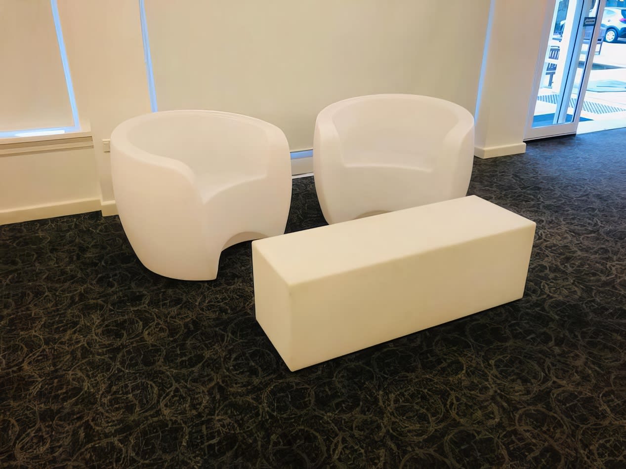 Two white chairs and a white ottoman in a room available for Glow Couch Hire.