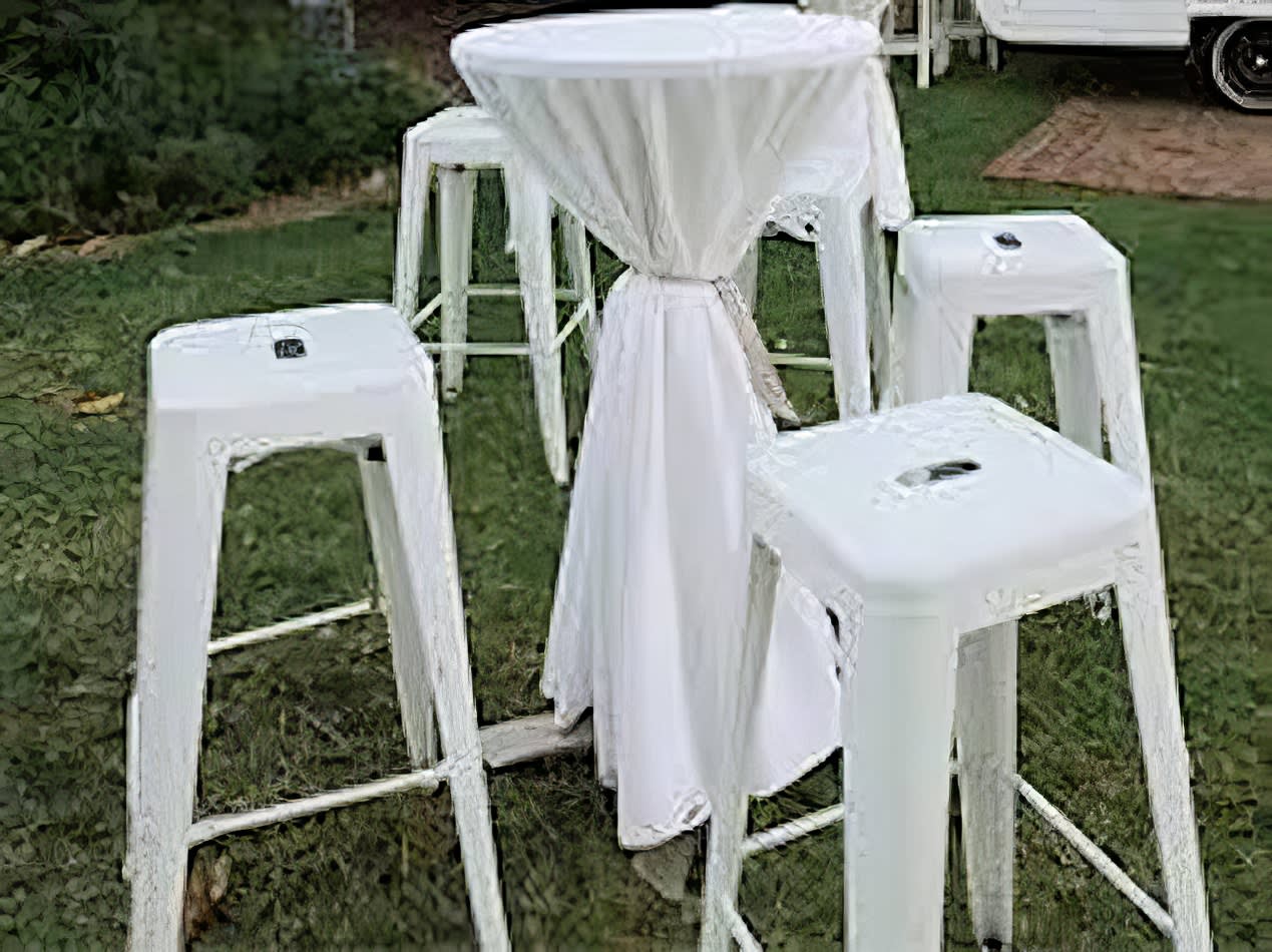 A set of white Tolix stools in a grassy area.