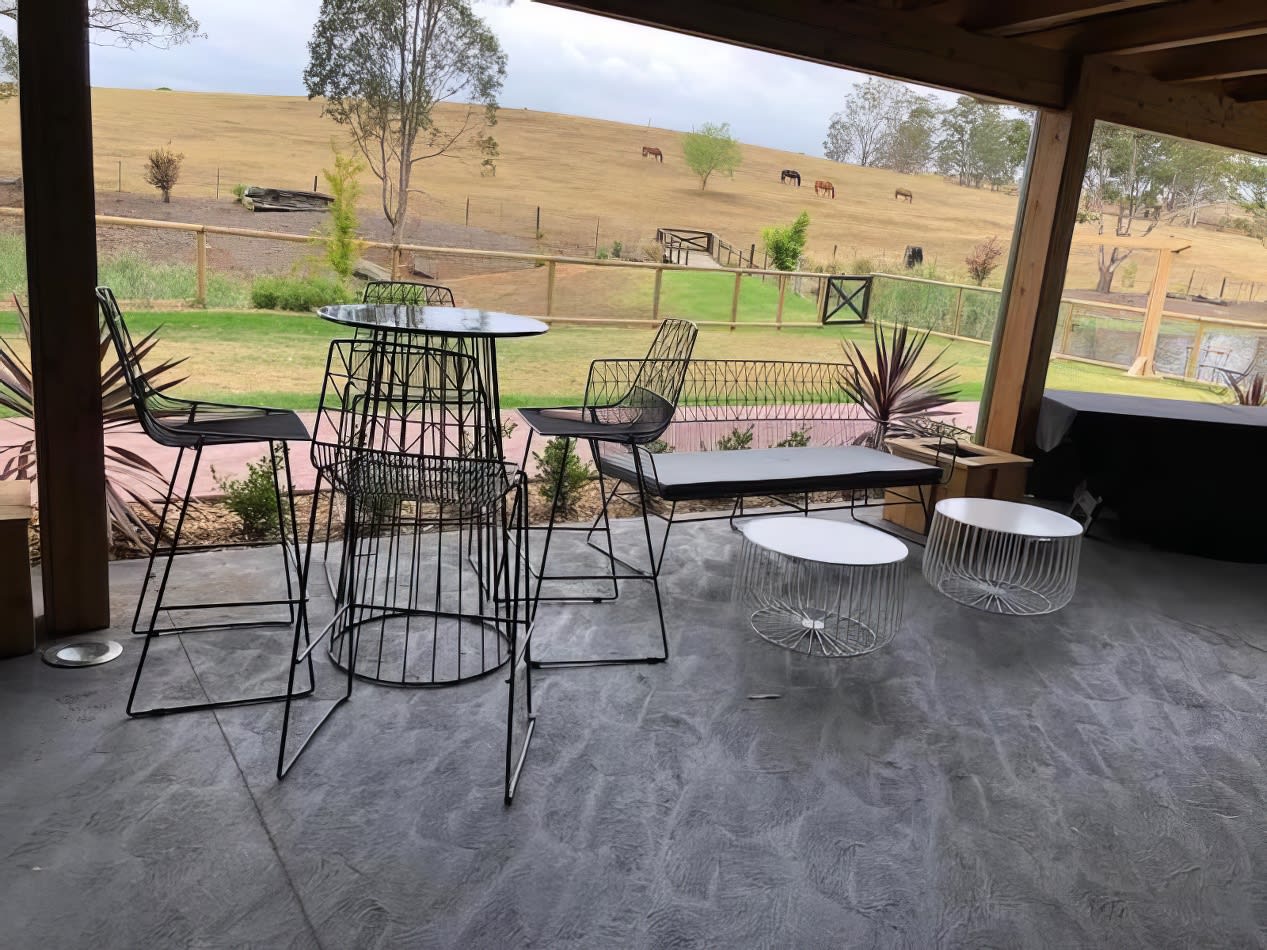 A white coffee table and chairs on a patio with a view of a field.