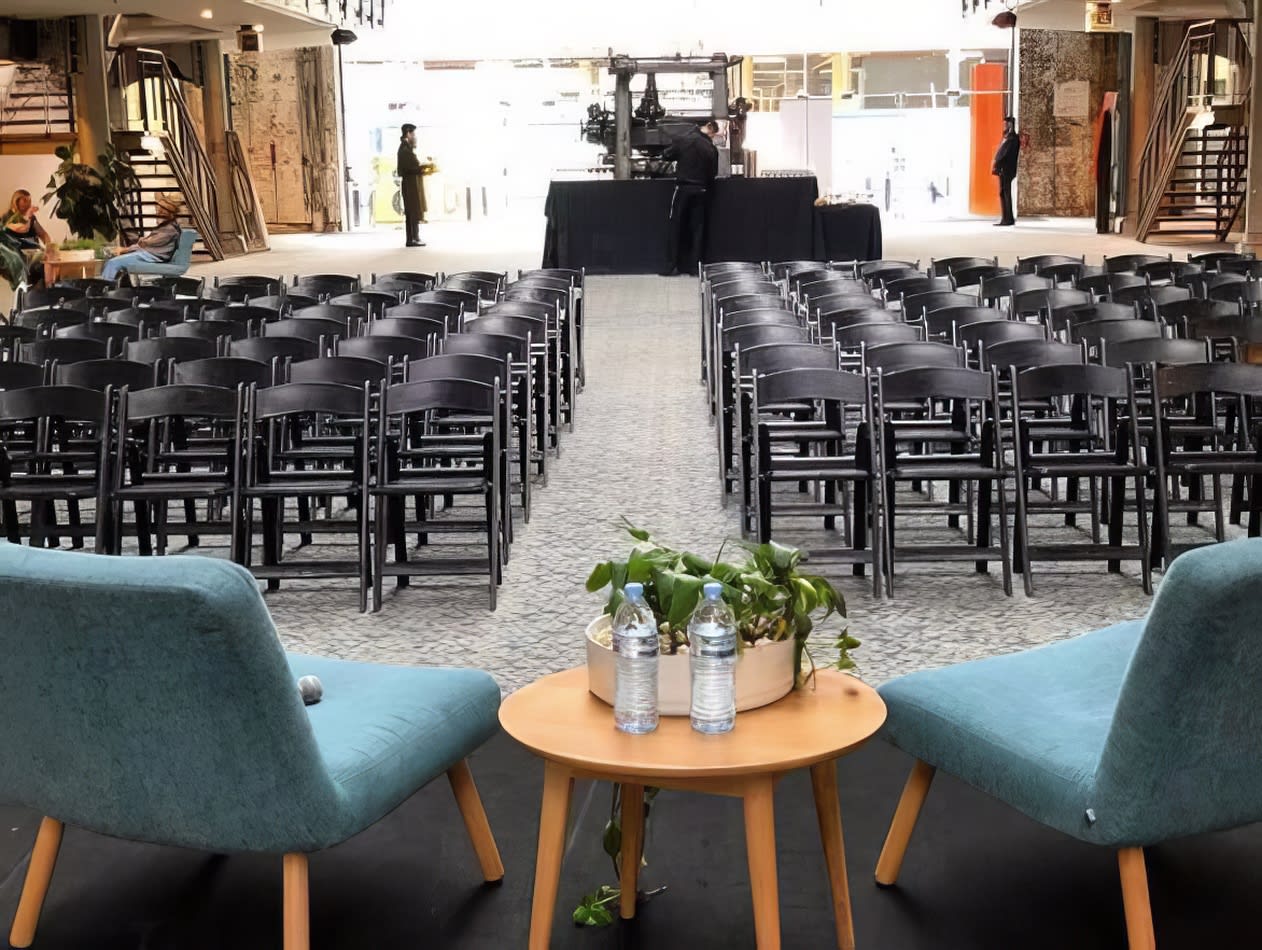 A room with black padded folding chairs and tables set up for a wedding.
