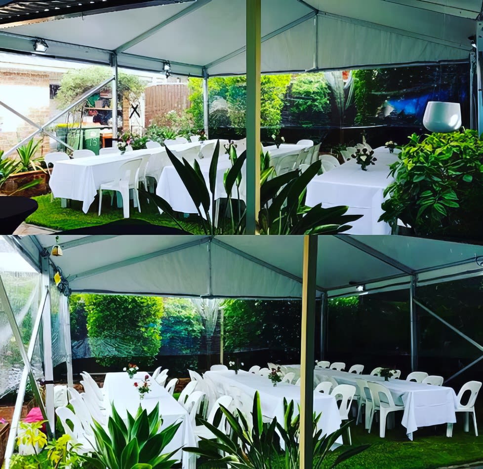 A white tent with tables and chairs set up in a garden, illuminated with LED floodlights.