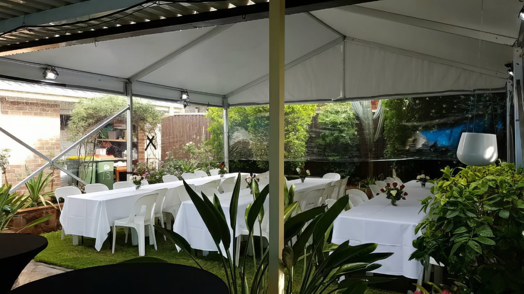 A white framed marquee tent with tables and chairs set up in a backyard.