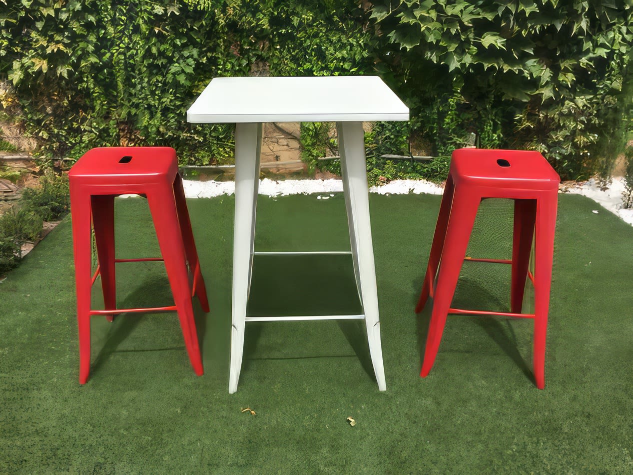 Two red Tolix stools and a table in a grassy area.