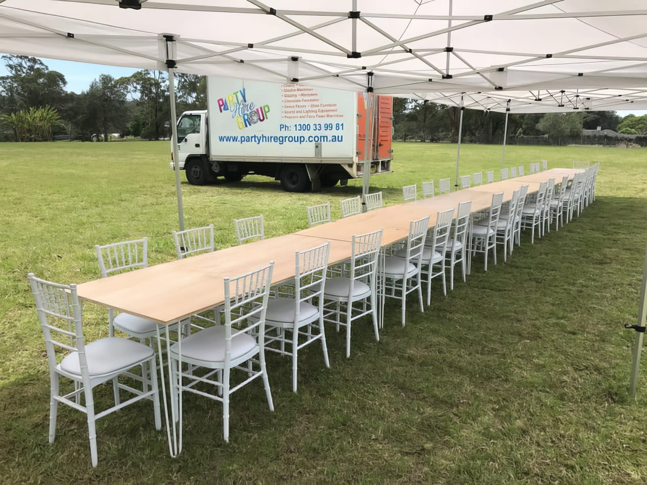 A long gold hairpin banquet table with white chairs, set under a tent.