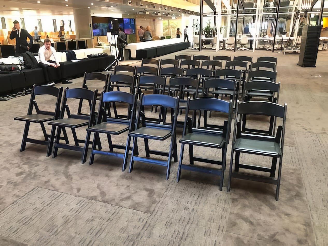 A row of black padded folding chairs in a lobby available for hire.