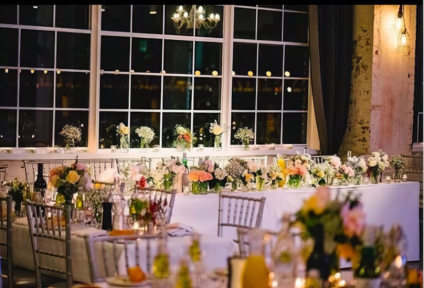 A table set up with flowers and candles in front of a window, enhanced with elegant silver Tiffany chairs.