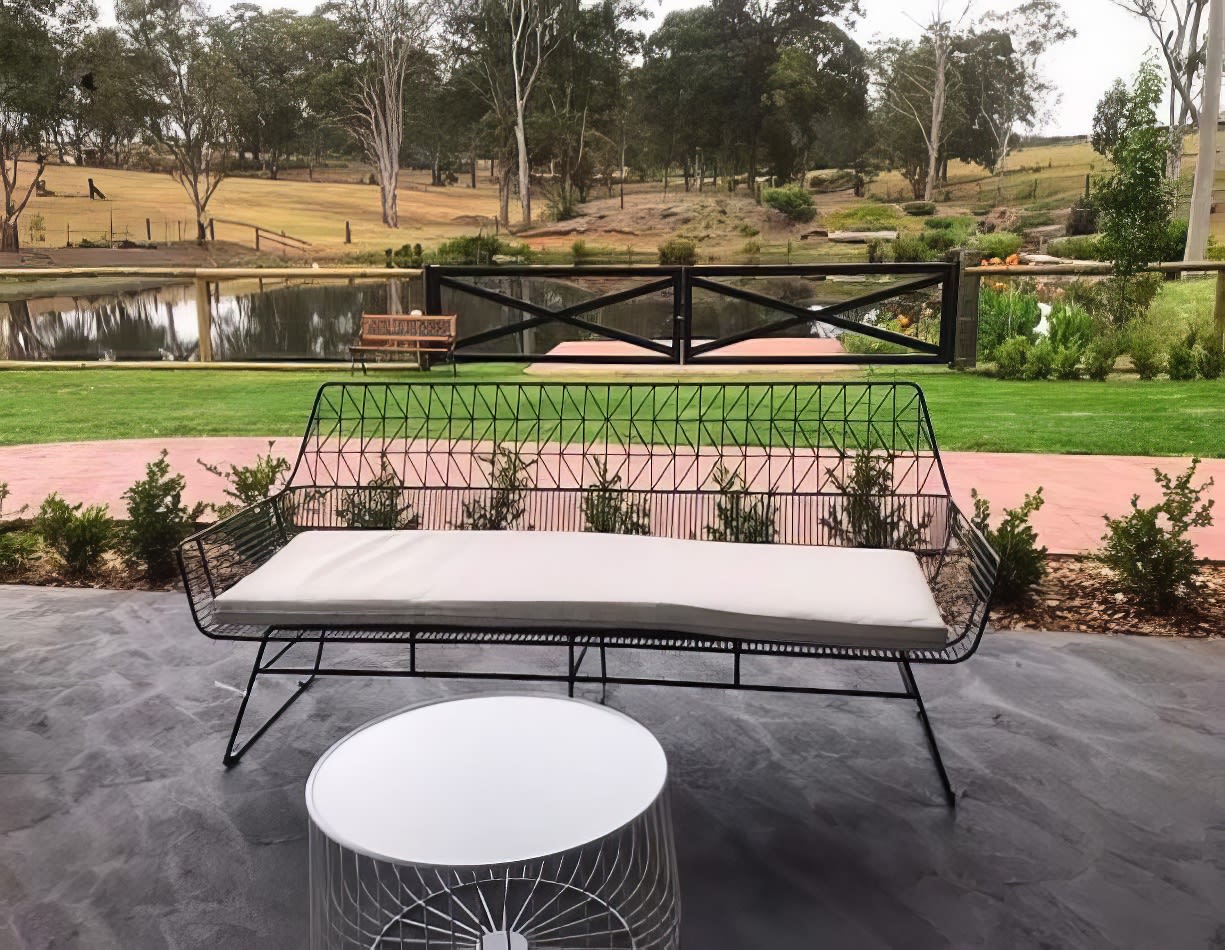 A patio with a bench and table next to a pond. The seating arrangement includes the elegant Black Arrow 3 Seater Lounge available for hire.