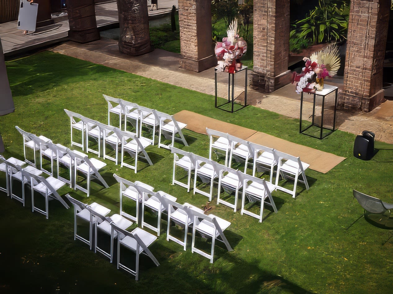 An outdoor wedding ceremony set up with white padded folding chairs.