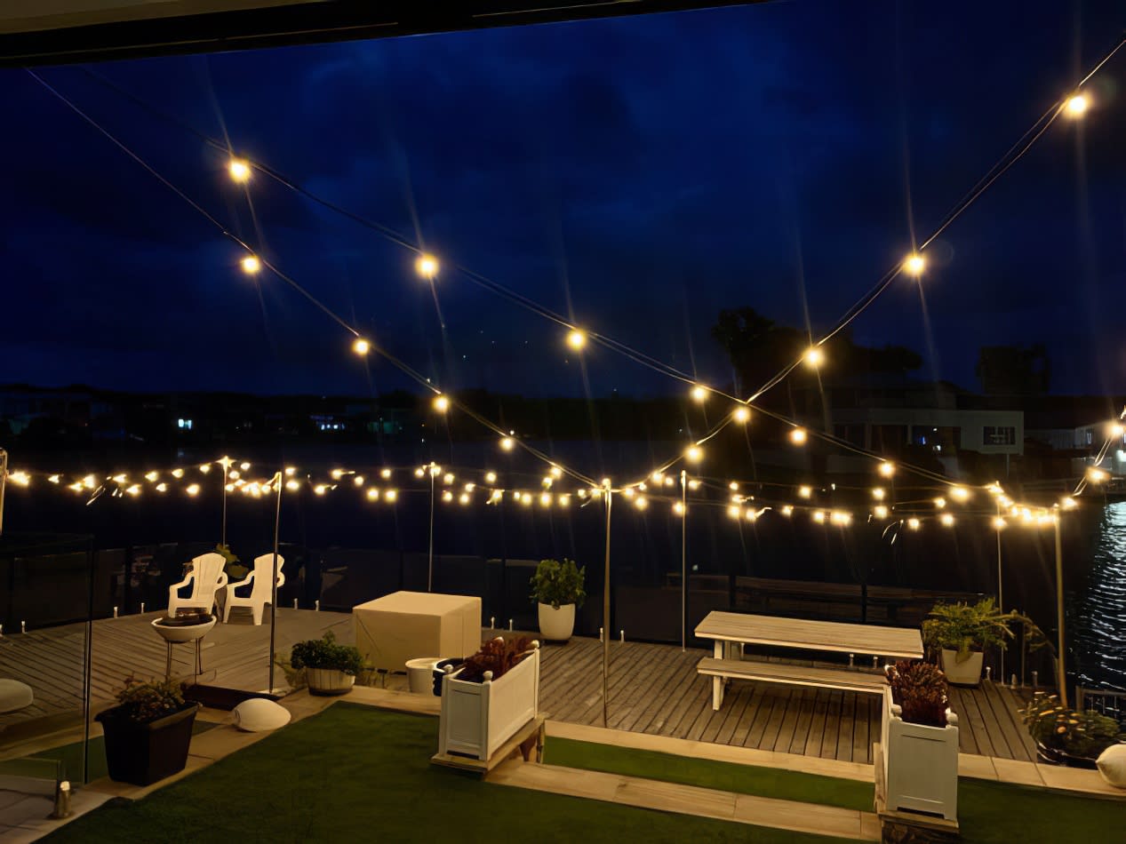 A deck with string lights and a view of the water illuminated by festoon light hire.