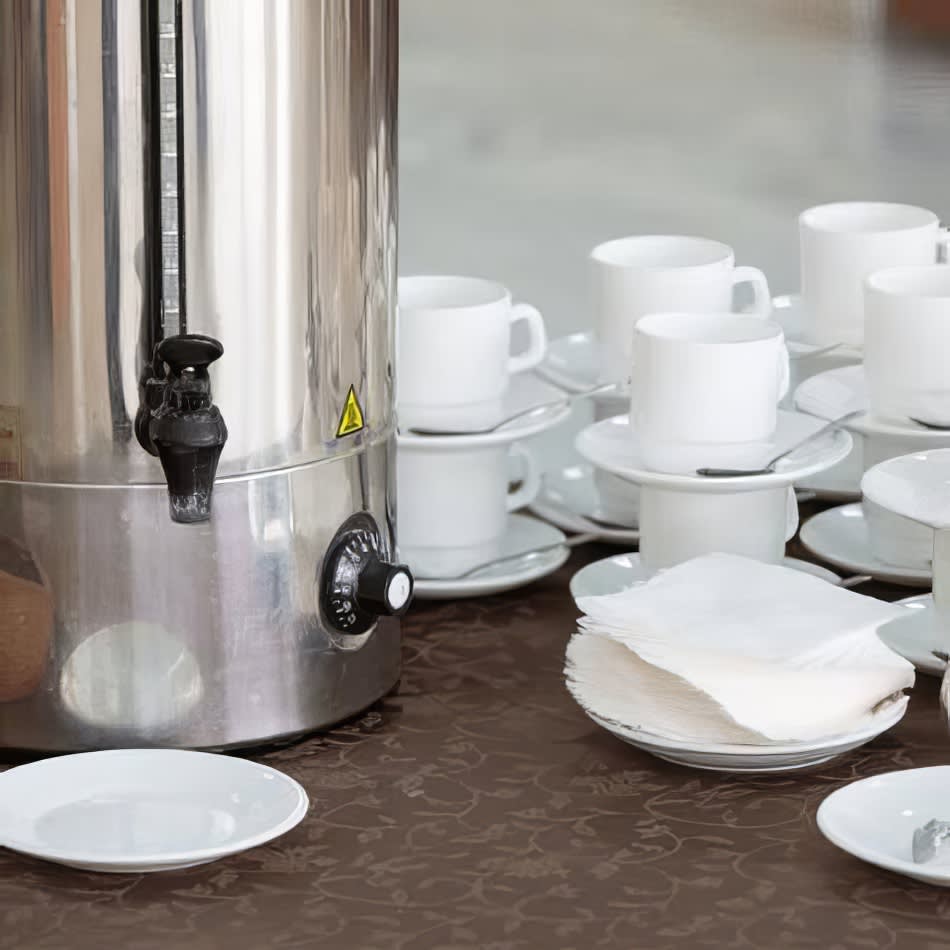 A 30L coffee urn with cups and saucers on a table.