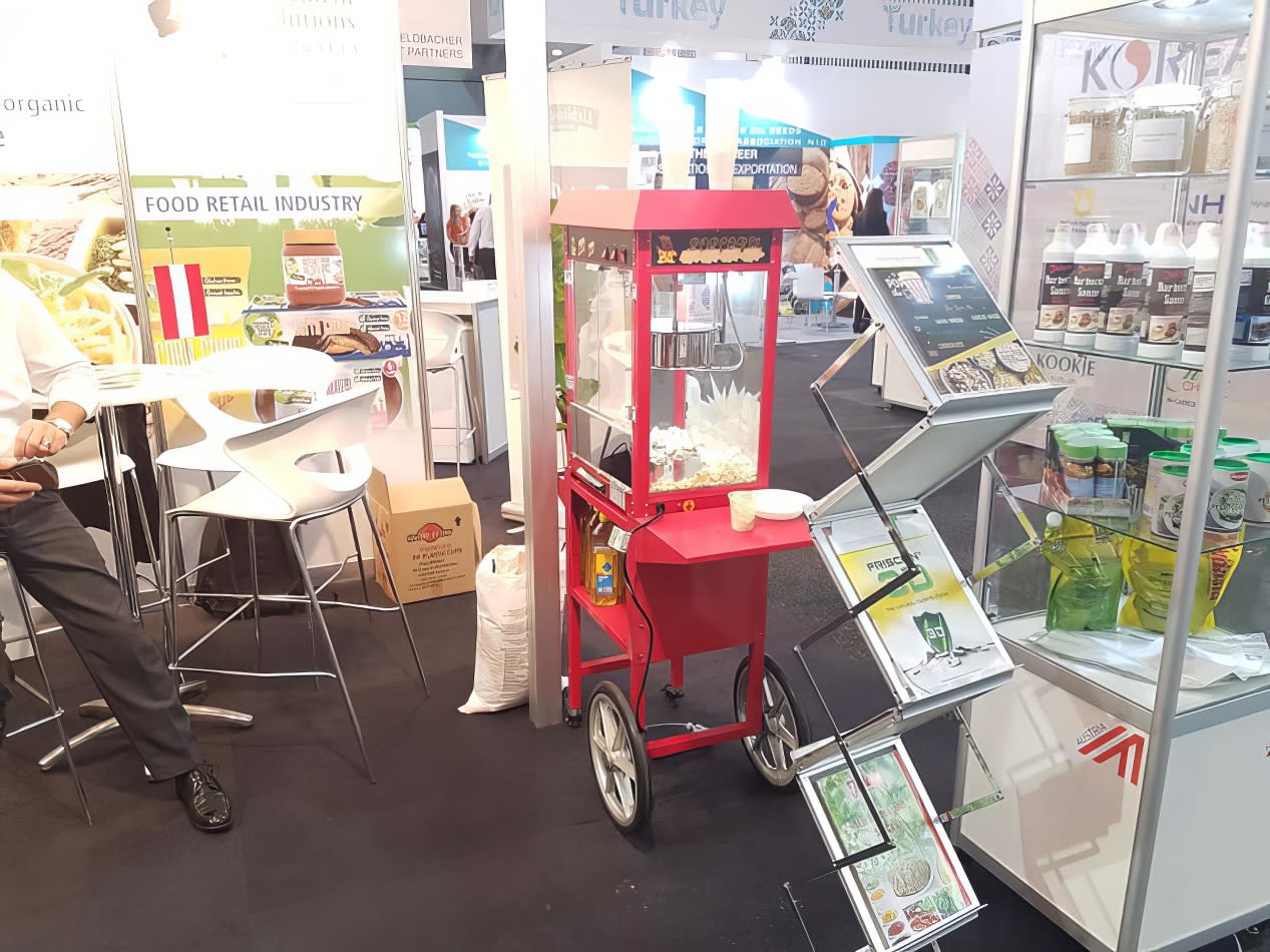 A man standing next to a popcorn cart at a trade show.
