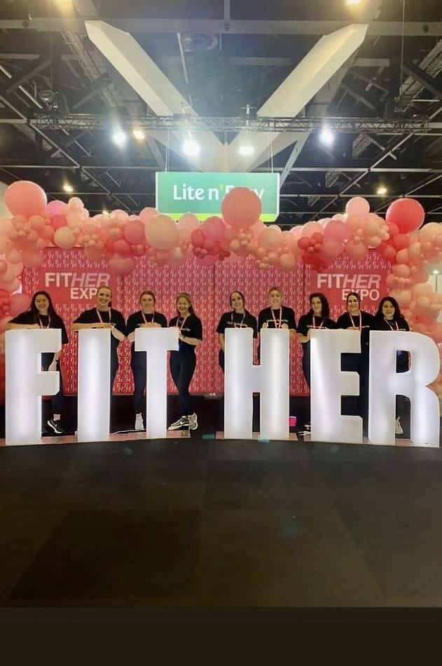 A group of people posing in front of a sign that says "fither" highlighted with glow letters.