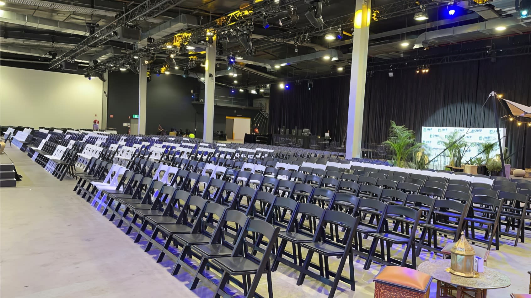 A large auditorium with rows of black padded folding chairs and lights.