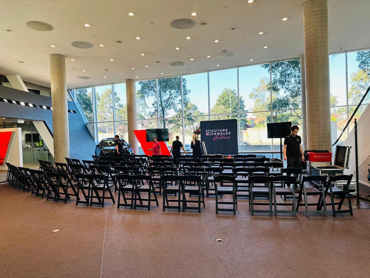 A room full of black padded folding chairs in a room with large windows.