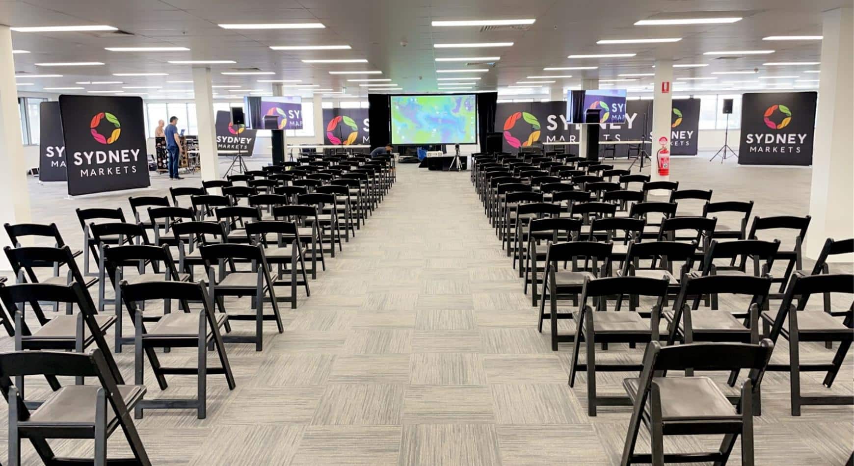 A large conference room with rows of chairs, including black padded folding chairs, and a projector.