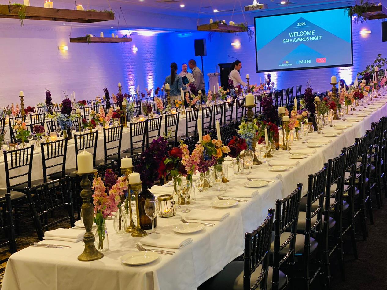 A large room with tables and chairs set up for an event, featuring Black Tiffany Chair Hire.