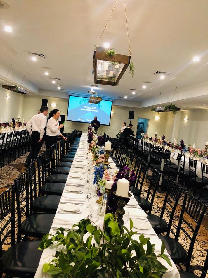 A long table is set up in a large room for a sophisticated event with black Tiffany chair hire available.