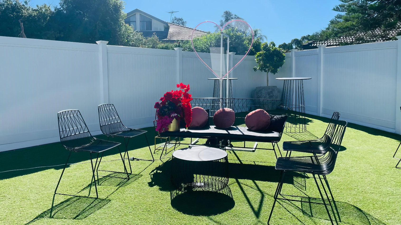 A backyard with black furniture and a white fence, featuring Black Wire Chair.