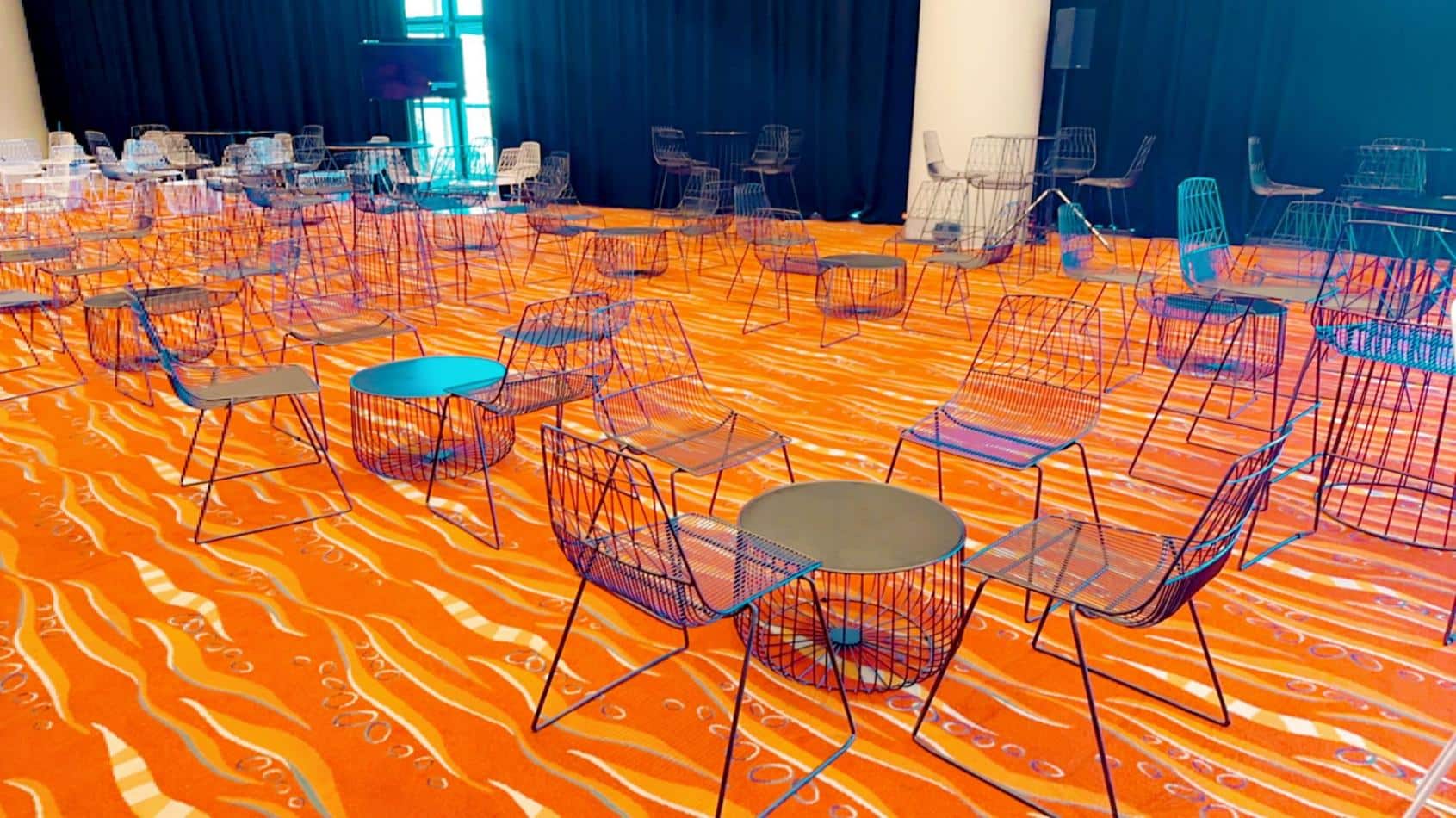 A room with chairs and tables on an orange floor, including Black Wire Chairs or Black Arrow Chair Hire options.