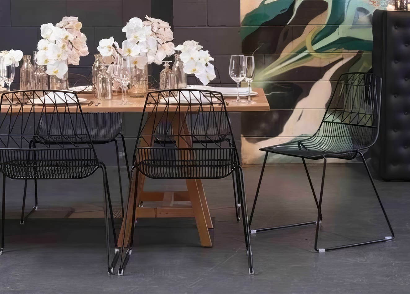 A dining table with black chairs and a painting on the wall. Black Arrow Chair Hire.