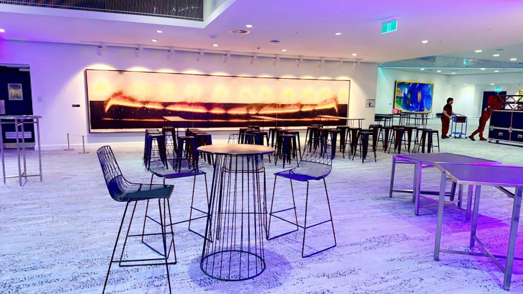 A bar with black wire stools and a painting on the wall.