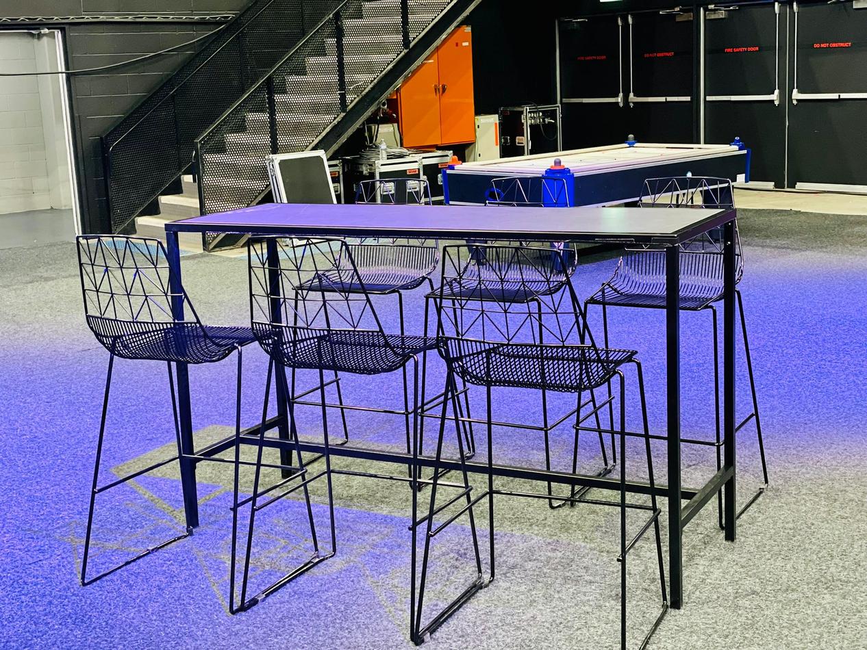 A bar table with four stools, including black wire stools for hire, and a basketball hoop.