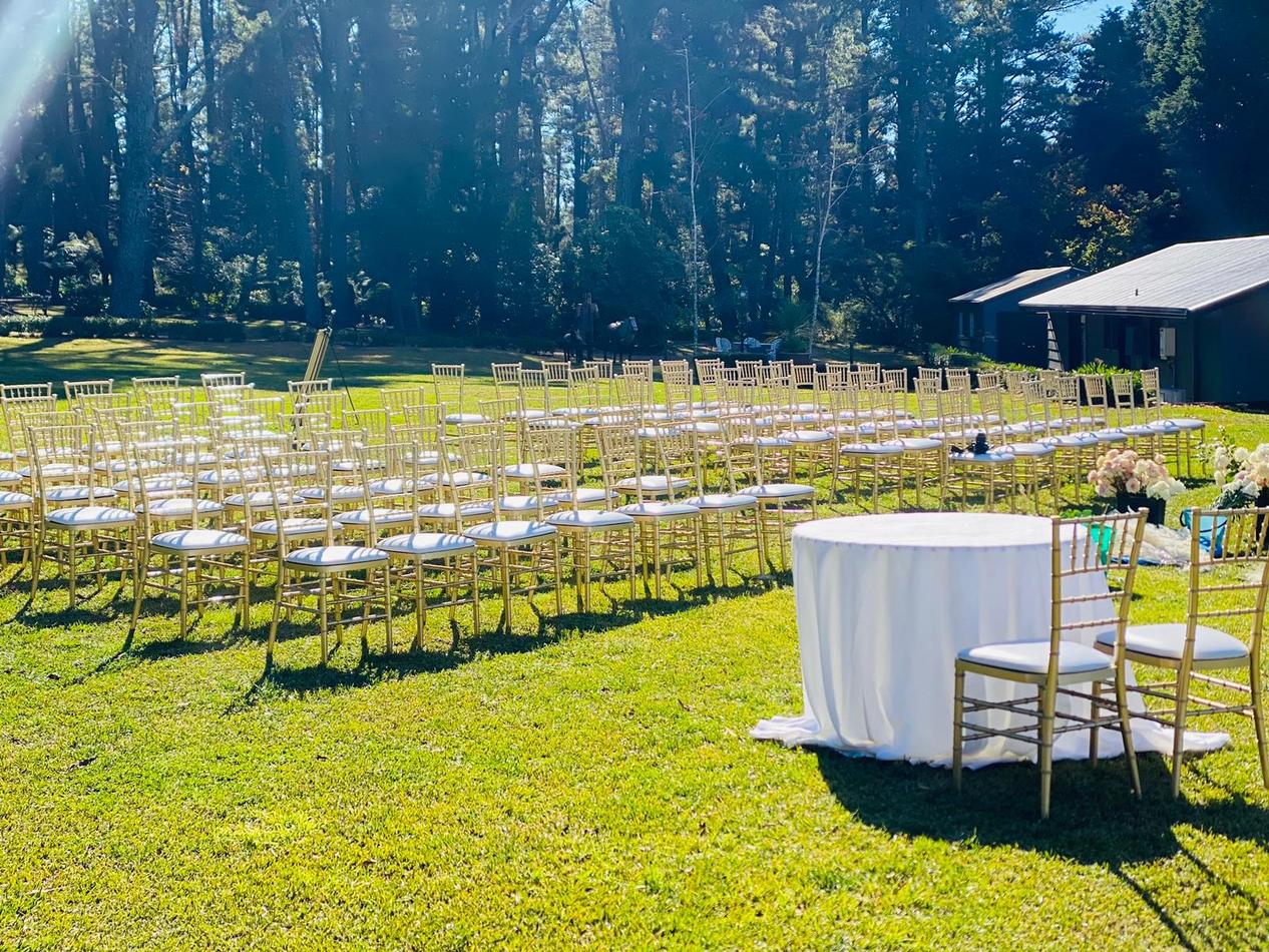 A wedding ceremony set up in a grassy field with Gold Tiffany Chair Hire.